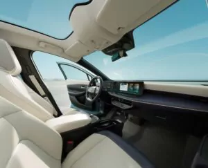 Das Bild zeigt den geräumigen, modernen Innenraum eines Autos mit weißen Ledersitzen, einem Panorama-Schiebedach, einem digitalen Armaturenbrett und großen Fenstern, die natürliches Licht vor dem Hintergrund eines klaren blauen Himmels hereinlassen.