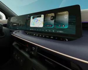 Großansicht eines modernen Auto-Armaturenbretts mit einem großen digitalen Bildschirm, auf dem Navigation, Fahrereinstellungen und Verbindungsoptionen über den Klimareglern und einem Gangwahlschalter angezeigt werden.