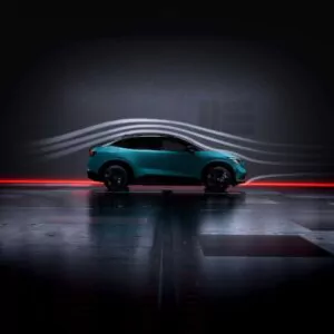 Ein tealfarbener Geländewagen wird im Profil in einem dunklen Raum gezeigt, wobei die aerodynamischen Luftstromlinien über und um das Fahrzeug herum hervorgehoben werden, um sein stromlinienförmiges Design zu betonen. Rotes Licht leuchtet unter dem Auto.