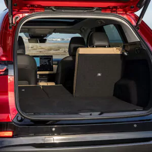 Die geöffnete Heckklappe eines roten SUVs, bei dem eine Rücksitzbank flach umgeklappt ist, gibt den Blick auf einen geräumigen Laderaum frei, der sich perfekt für Ihr nächstes Abenteuer eignet. Der schwarze Innenraum mit hellbraunen Akzenten unterstreicht den modernen Stil des Fahrzeugs, während der gut sichtbare Touchscreen im Armaturenbrett auf fortschrittliche technische Funktionen hindeutet. Diese Szene verdeutlicht perfekt, warum das Leasing eines Mazda CX-5 eine attraktive Option für alle ist, die sowohl Vielseitigkeit als auch Raffinesse suchen.