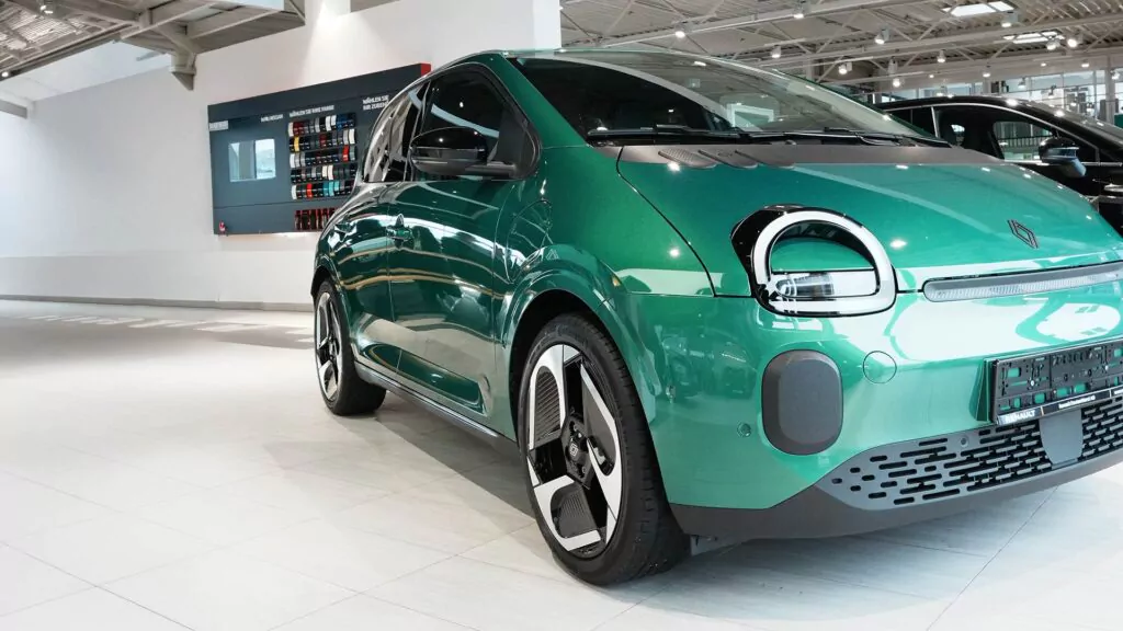 Ein leuchtend grünes Elektroauto ist in einem hell erleuchteten Ausstellungsraum mit weißen Böden und Wänden geparkt, und im Hintergrund ist eine moderne Einrichtung zu sehen.