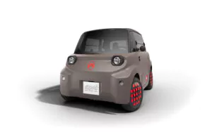 Ein kleines, kompaktes, graues Elektroauto mit rundem Design und roten Akzenten an den Rädern, von vorne links gesehen vor weißem Hintergrund. Die Vorderseite zeigt runde Scheinwerfer und ein Logo über dem Nummernschild mit der Aufschrift ami.