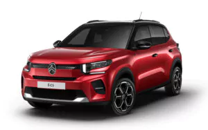 Ein roter Citroën ë-C3 Elektro-SUV wird in einer Studioumgebung gezeigt, von vorne links gesehen. Das Fahrzeug verfügt über schwarze Dachakzente, moderne LED-Scheinwerfer und einen markanten Citroën-Kühlergrill.