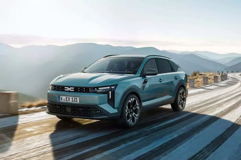 Ein blauer Dacia Striker fährt auf einer kurvenreichen Bergstraße mit Steinbarrieren, malerischen Bergen und einem klaren Himmel im Hintergrund.