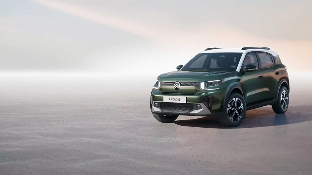 Ein grüner Citroën Aircross Geländewagen mit weißem Dach ist auf einer offenen, leeren Fläche geparkt, mit einem weichen, pastellfarbenen Himmel im Hintergrund.