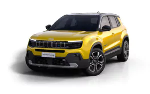 Ein gelber Jeep Avenger, ein kompakter Geländewagen, ist auf einem weißen Hintergrund abgebildet, von vorne links gesehen, mit seinem charakteristischen Kühlergrill, dem schwarzen Dach und den eleganten Leichtmetallrädern.