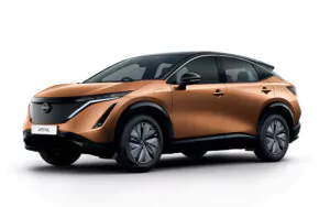 Ein bronzener Nissan Ariya Elektro-SUV wird von vorne gezeigt, mit schlanken Linien, schwarzen Dachakzenten und modernen LED-Scheinwerfern auf weißem Hintergrund.