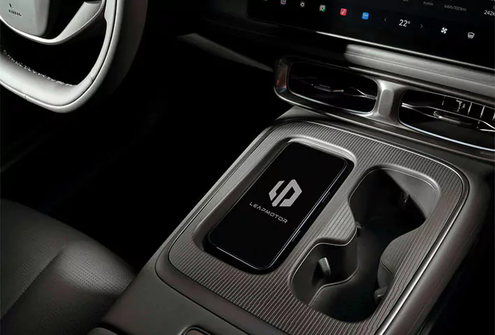 Eine Nahaufnahme der Mittelkonsole eines Autos zeigt eine kabellose Ladestation mit einem Smartphone, auf dem das Leapmotor-Logo zu sehen ist, neben zwei Getränkehaltern und einem Teil des Armaturenbrett-Displays – ein Blick auf die intelligenten Funktionen, die das neueste Leapmotor B05-Angebot bietet.