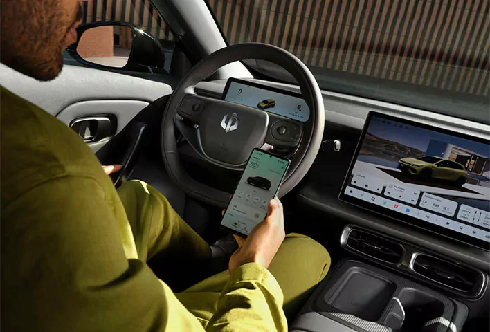 Eine Person in grüner Kleidung sitzt in einem modernen Leapmotor B05 und hält ein Smartphone in der Hand, auf dem eine Auto-App geöffnet ist. Das Armaturenbrett verfügt über zwei große Bildschirme, auf denen das Fahrzeug und verschiedene Bedienelemente zu sehen sind, wodurch die innovativen Funktionen dieses exklusiven Leapmotor B05-Angebots hervorgehoben werden.