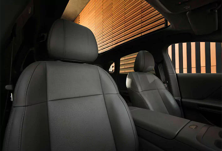 Zwei schwarze Ledersitze im vorderen Bereich eines modernen Leapmotor B05 mit elegantem Innendesign, vom Rücksitz aus gesehen; durch die Fenster ist eine orangefarbene Wand mit geometrischen Mustern zu sehen – eine stilvolle Kulisse, die den Reiz dieses Leapmotor B05-Angebots unterstreicht.