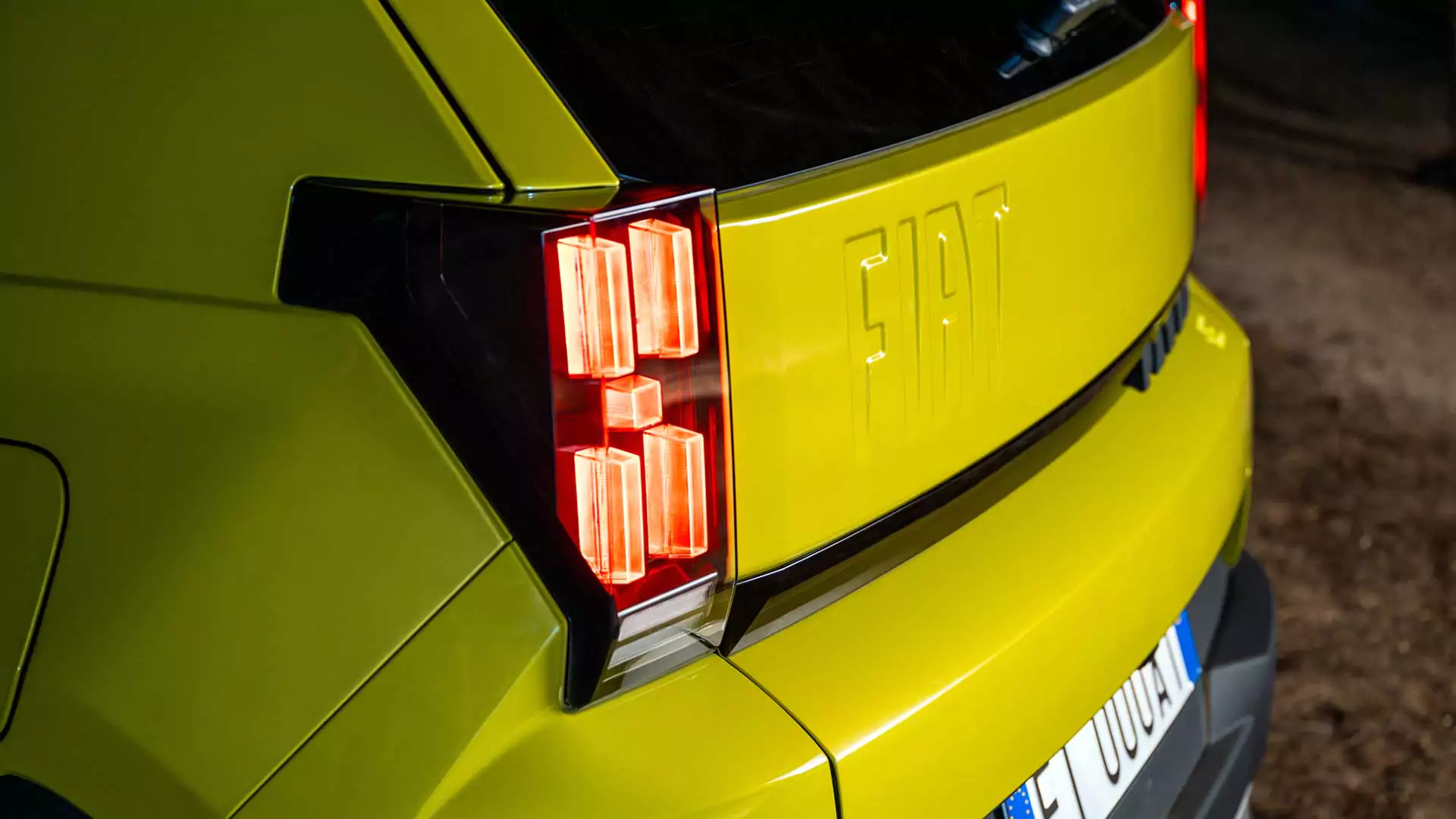 Nahaufnahme der linken Heckseite eines gelben Fiat, die das beleuchtete Rücklicht, das geprägte FIAT-Logo auf dem Kofferraum sowie einen Teil des Kennzeichens zeigt.