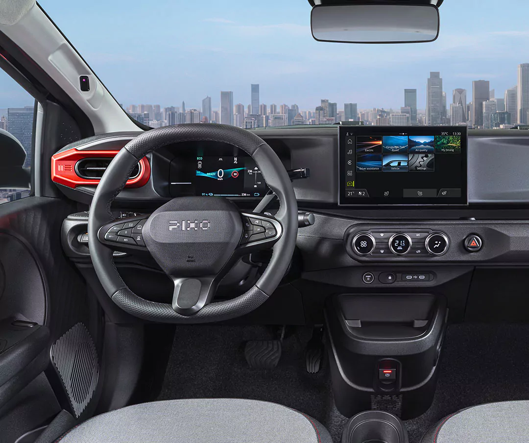 Der Innenraum eines modernen Nissan Pixo zeigt ein Lenkrad, ein digitales Armaturenbrett, einen Touchscreen, die Klimaregelung und eine Stadtlandschaft, die durch die Windschutzscheibe zu sehen ist. Das Design ist elegant und in Schwarz- und Grautönen gehalten.